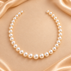 A single strand pearl necklace arranged in a loose arc on a soft champagne satin background.