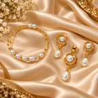 Gold jewelry set with white pearls, including a bracelet, earrings, and pendant, arranged on draped champagne satin fabric with small white flowers.