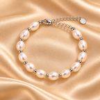 A pearl beaded bracelet with silver-toned metal beads and a chain clasp, displayed on a draped champagne satin fabric background.